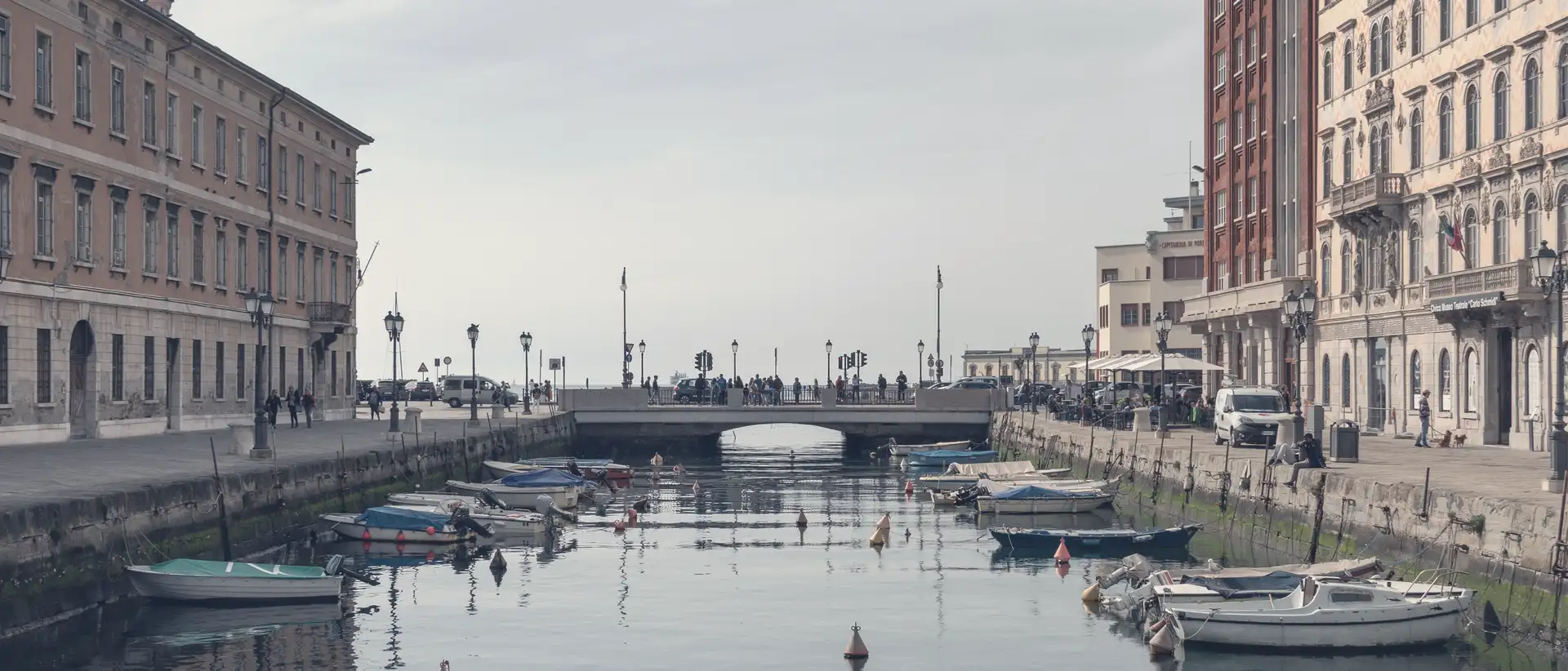 Trieste's Canal Grande with moored boats, buildings on both sides and the bridge at the end.