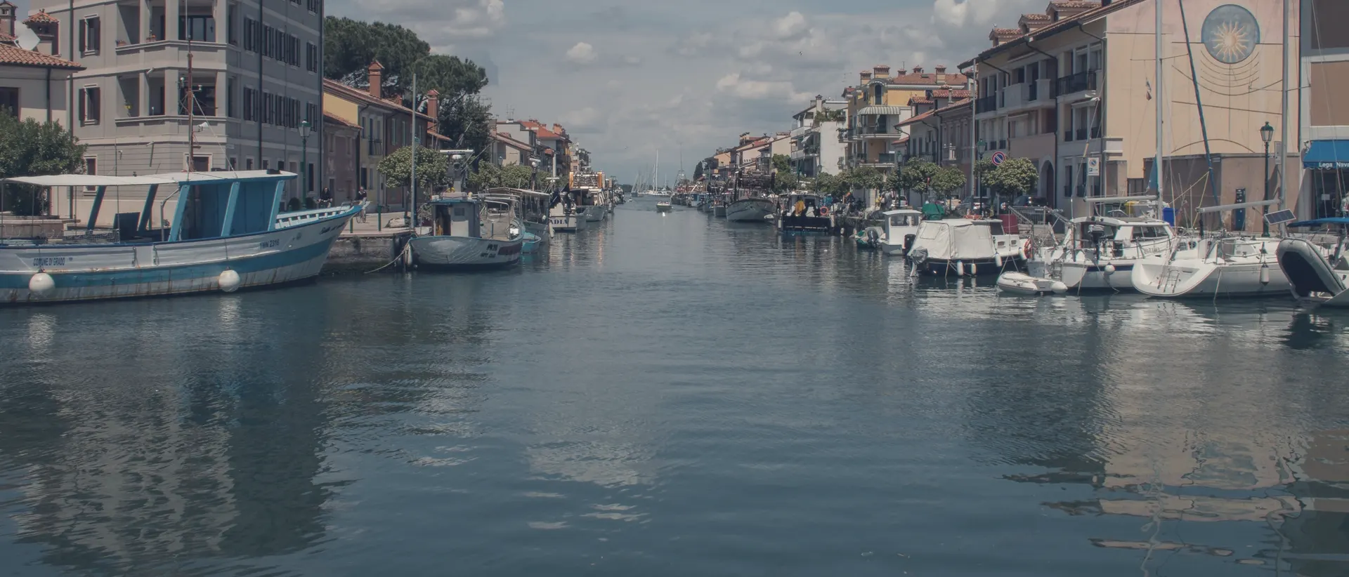 Der Kanalhafen von Grado mit vertäuten Booten und bunten Häusern am Ufer.