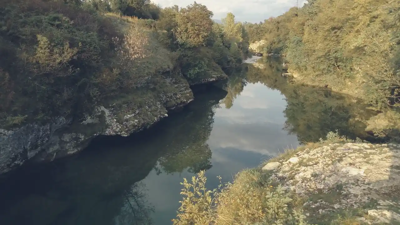 The Natisone gorge in autumn: green water between pale rocks and yellow trees.