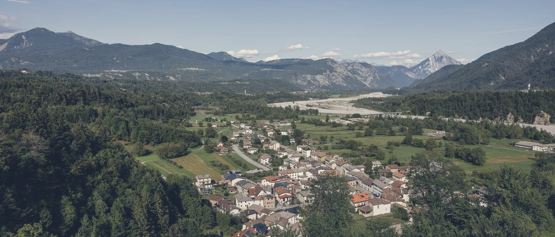 Das Tal des Tagliamento von oben: das Dorf Socchieve, das Flussbett und die Berge mit tiefen Wolken an den Graten.